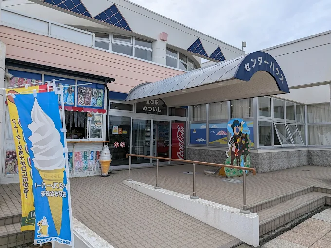 Entrance of a building with a blue canopy sign in Japanese, an ice cream cone banner, and a vending machine inside.