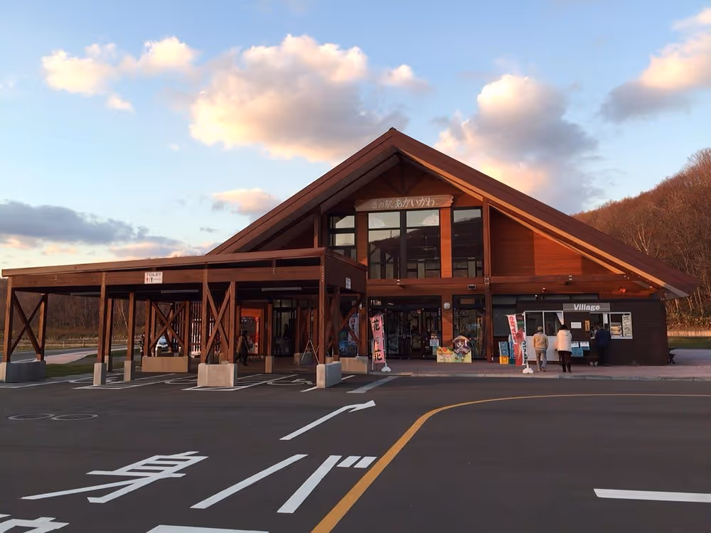 Wooden travel station building with a large triangular roof at sunset and parking spaces in front with Japanese road markings.
