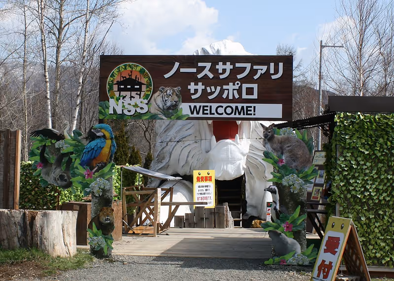 Entrance to North Safari Sapporo with large white tiger mouth sculpture and wooden sign featuring animals and welcome message.