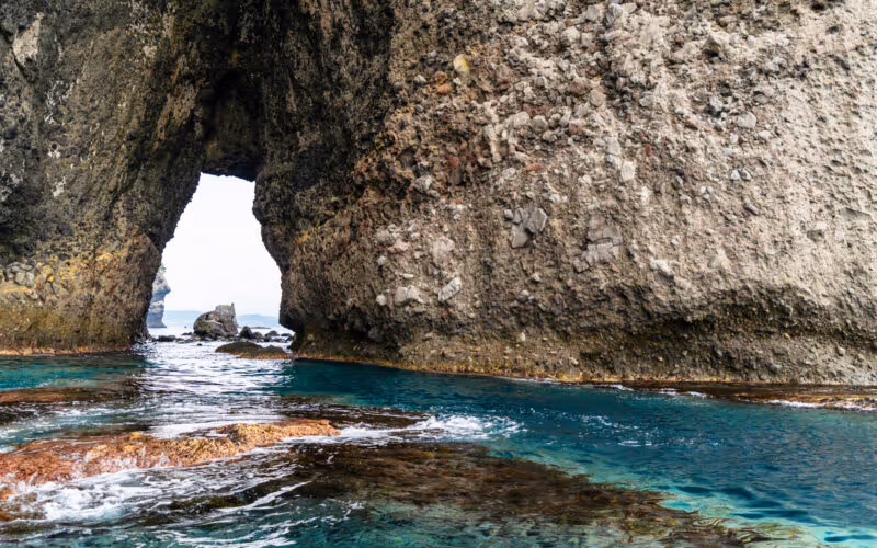 Clear turquoise water flowing through a natural rock arch formation by the sea.