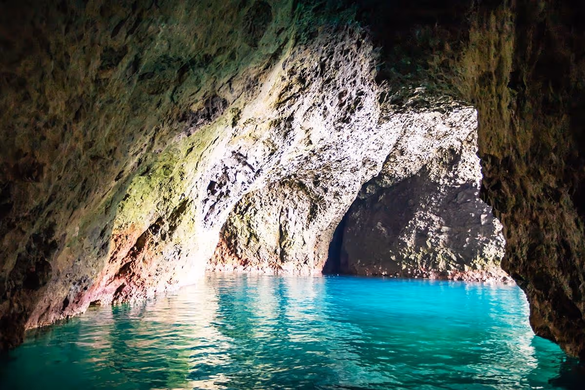 Bright turquoise water inside a rocky sea cave illuminated by natural light.