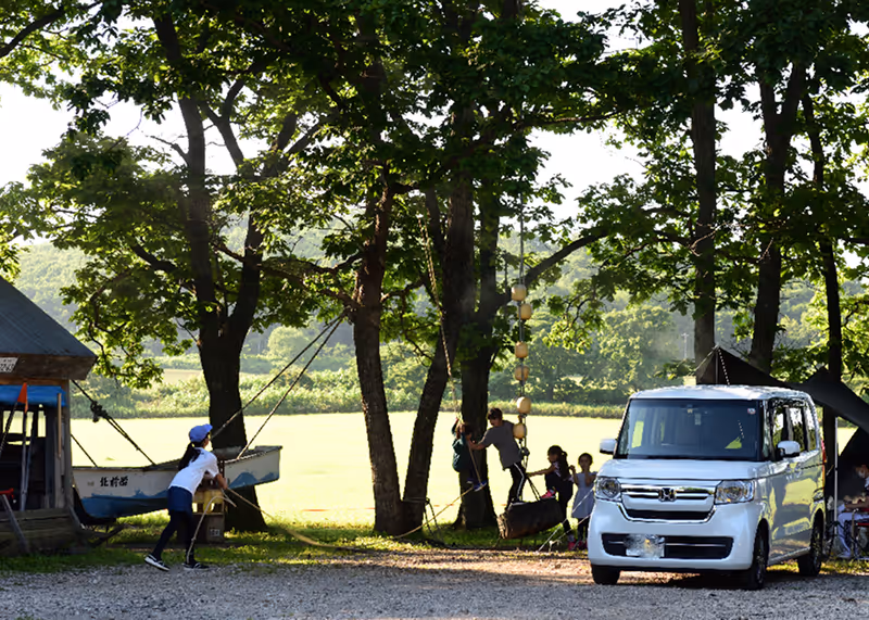 Group of children playing on a tire swing hanging from a tree near a white car and cabin in a wooded campsite.