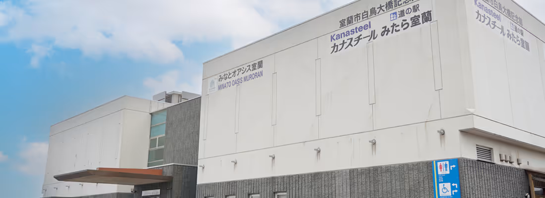 Modern building with signage reading Minato Oasis Muroran and Kanasteel under a partly cloudy sky.