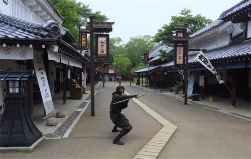 Ninja in black attire crouching in a traditional Japanese village street with wooden buildings and lanterns.