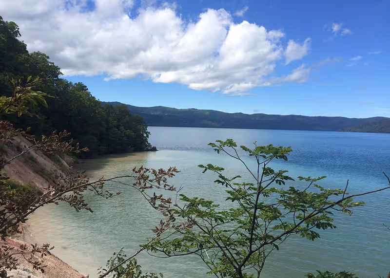 Calm blue lake bordered by green forested hills under a partly cloudy sky.