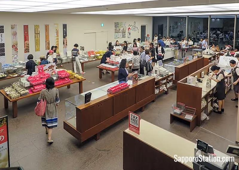 Interior view of a bustling Japanese store with several customers shopping and cashiers assisting at counters.