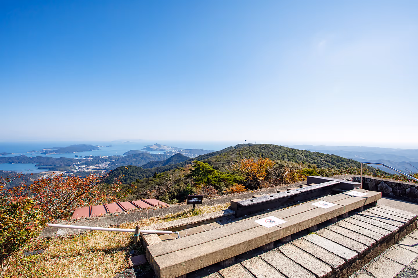 Mountain summit observation area with benches overlooking islands and a clear blue sky.