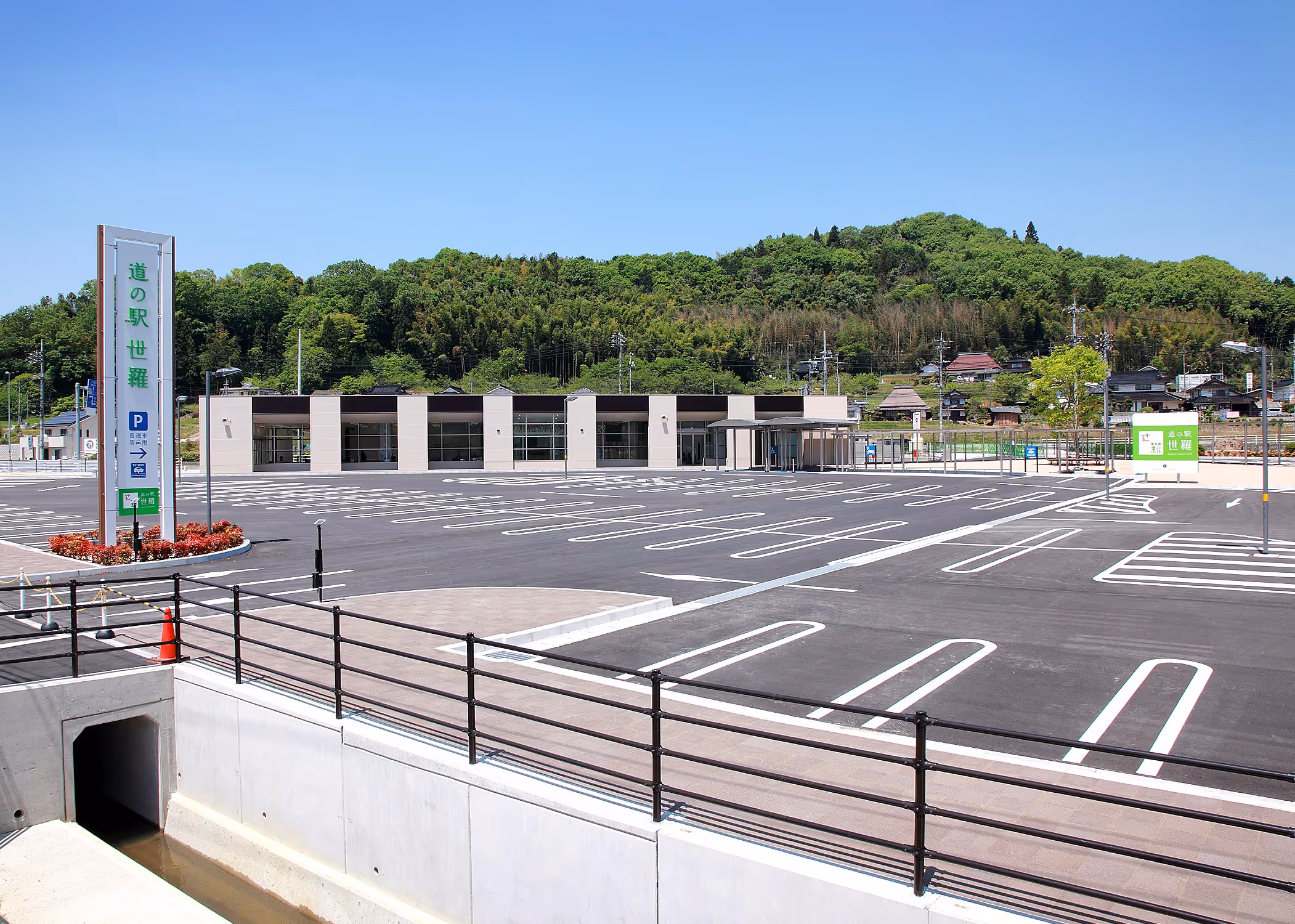 Empty parking lot and modern building of Roadside Station Sera surrounded by greenery under blue sky.