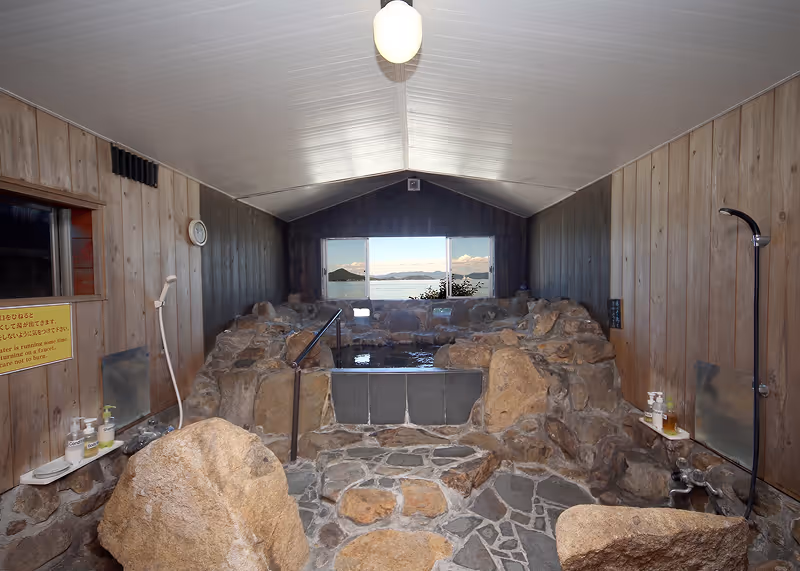 Dark blue compact car parked on a dirt lot beside white residential buildings with trees and hills in the background.