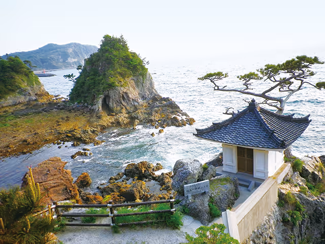Coastal rocky landscape with a small traditional Japanese shrine and a pine tree overlooking the ocean.