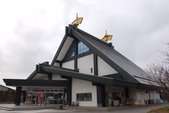 Building with steeply sloped roof and two golden ornaments on top under a cloudy sky.