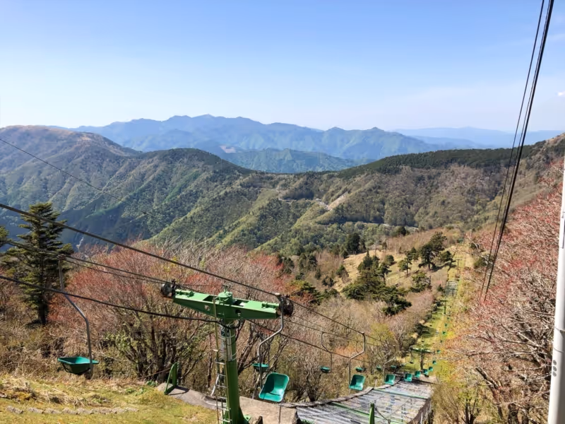 Mountain chairlift with green seats ascending a forested hillside under a clear blue sky.