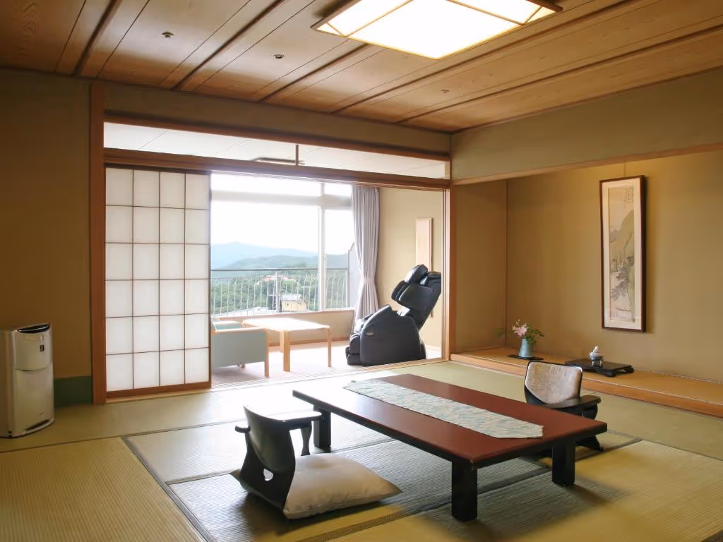 Traditional Japanese tatami room with low wooden table, floor chairs, shoji sliding door, and a massage chair near a window with mountain views.