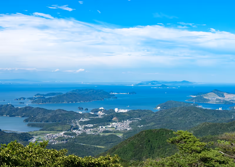 Scenic view of a coastal area with green hills, small islands, and blue ocean under a partly cloudy sky.