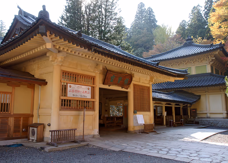 Traditional Japanese building with wooden lattice windows and tiled roof surrounded by tall trees and autumn foliage.