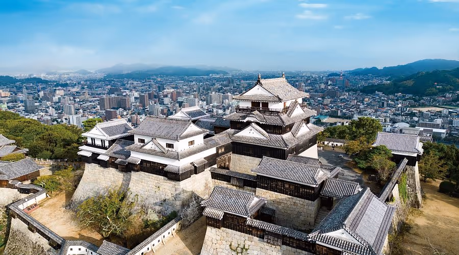 Aerial view of Matsuyama Castle with traditional Japanese architecture overlooking the city and surrounding hills.