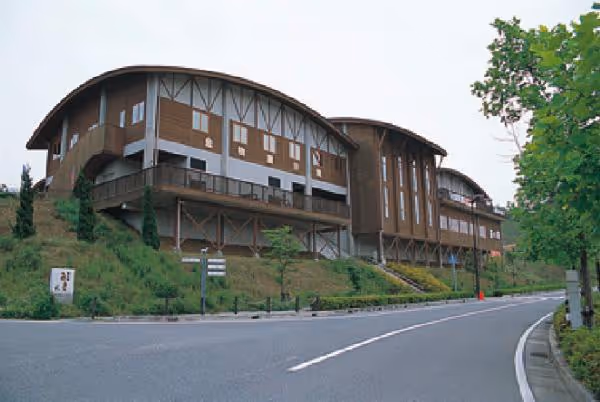 Curved-roof building on a small hill beside a curved road with trees and greenery.