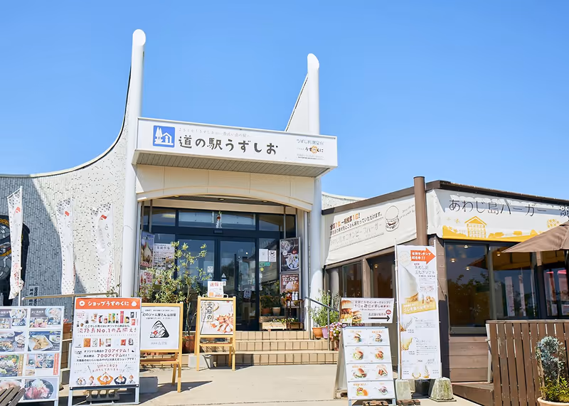 Entrance of a Japanese roadside station with signage, outdoor menus, and clear blue sky.