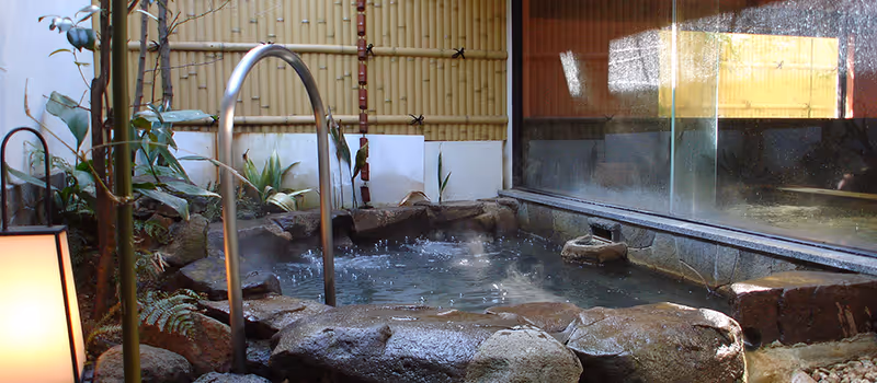 Steaming stone outdoor hot spring bath with bamboo fence and glass wall panels.