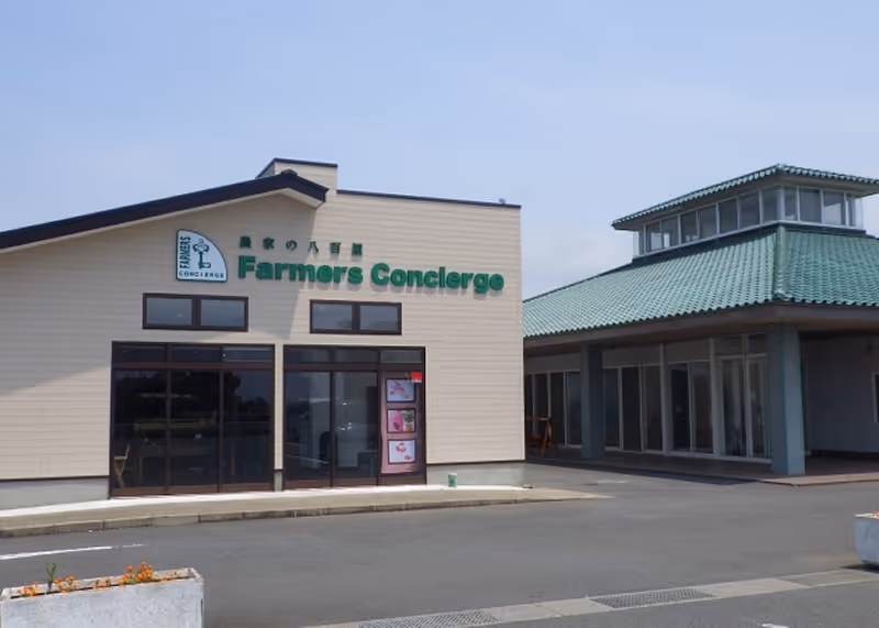 Modern building with green signage reading 'Farmers Concierge' and an adjacent structure with a green tiled roof under a clear sky.