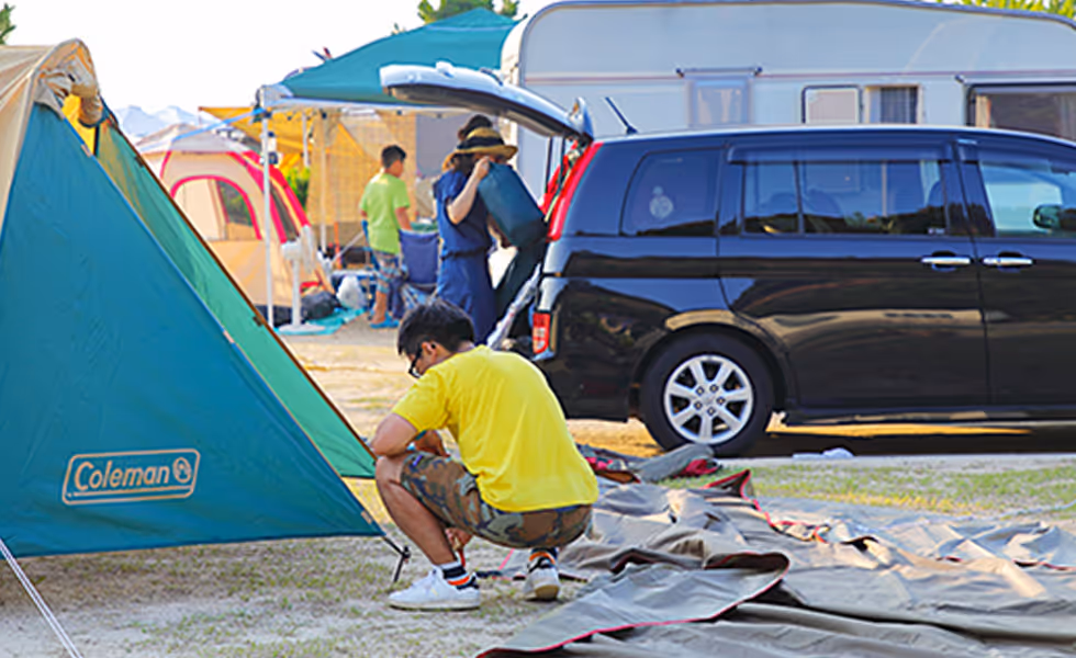 People setting up tents and camping gear near a black van and a trailer during daylight.