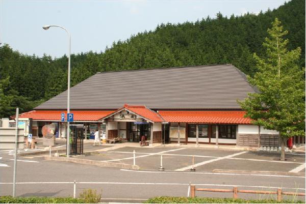 Large traditional-style building with a gray roof and red accent roof, surrounded by a parking area and forest trees.