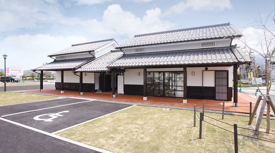 Traditional Japanese style building with tiled roof and white walls next to a handicapped parking space under a partly cloudy sky.