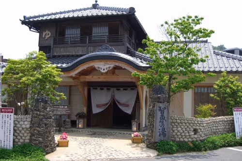 Traditional Japanese onsen building with tiled roof, wooden entrance, and a white curtain hanging over doorway.