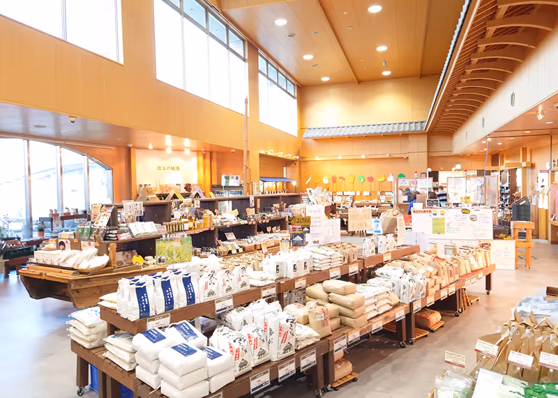 Bright interior of a Japanese market with wooden shelves filled with bags of rice and local products.