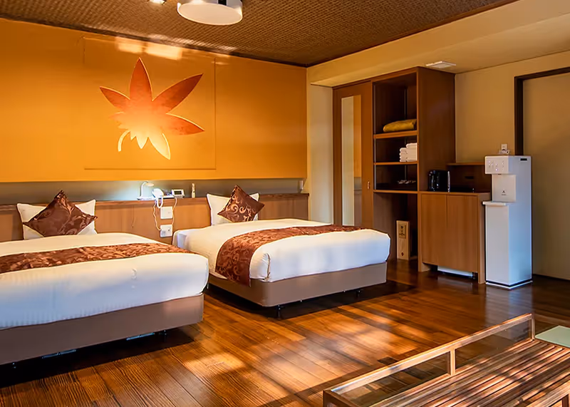 Modern hotel room with two beds featuring white and brown linens, a wooden floor, and a large wall decoration of a maple leaf.