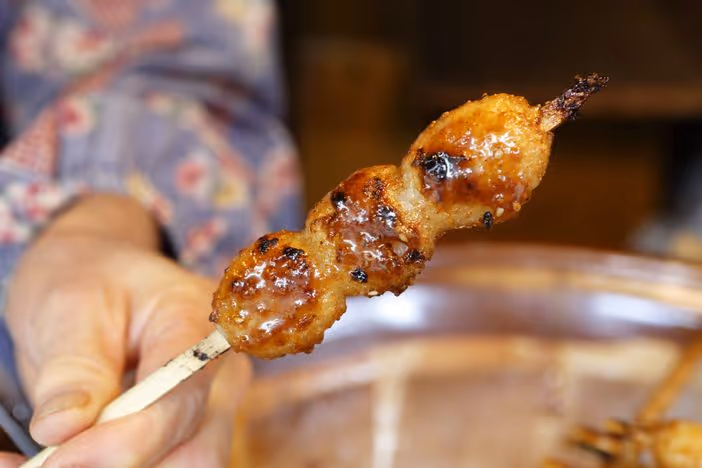 Hand holding a skewer with three grilled, glazed dango balls.