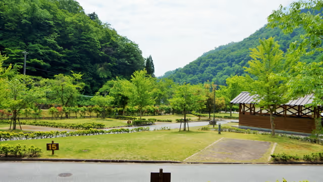 Grassy campsite area with numbered plots, surrounded by lush green trees and hills under a partly cloudy sky.
