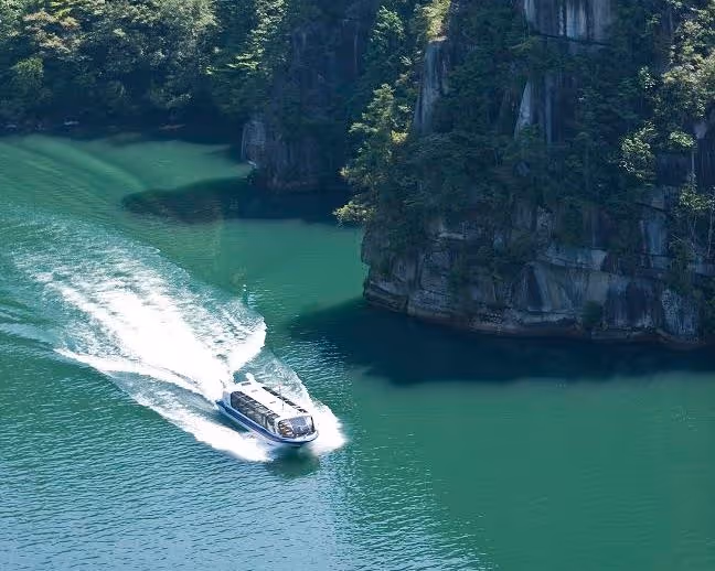 Boat cruising on emerald green water near steep, forested cliffs in a scenic gorge.