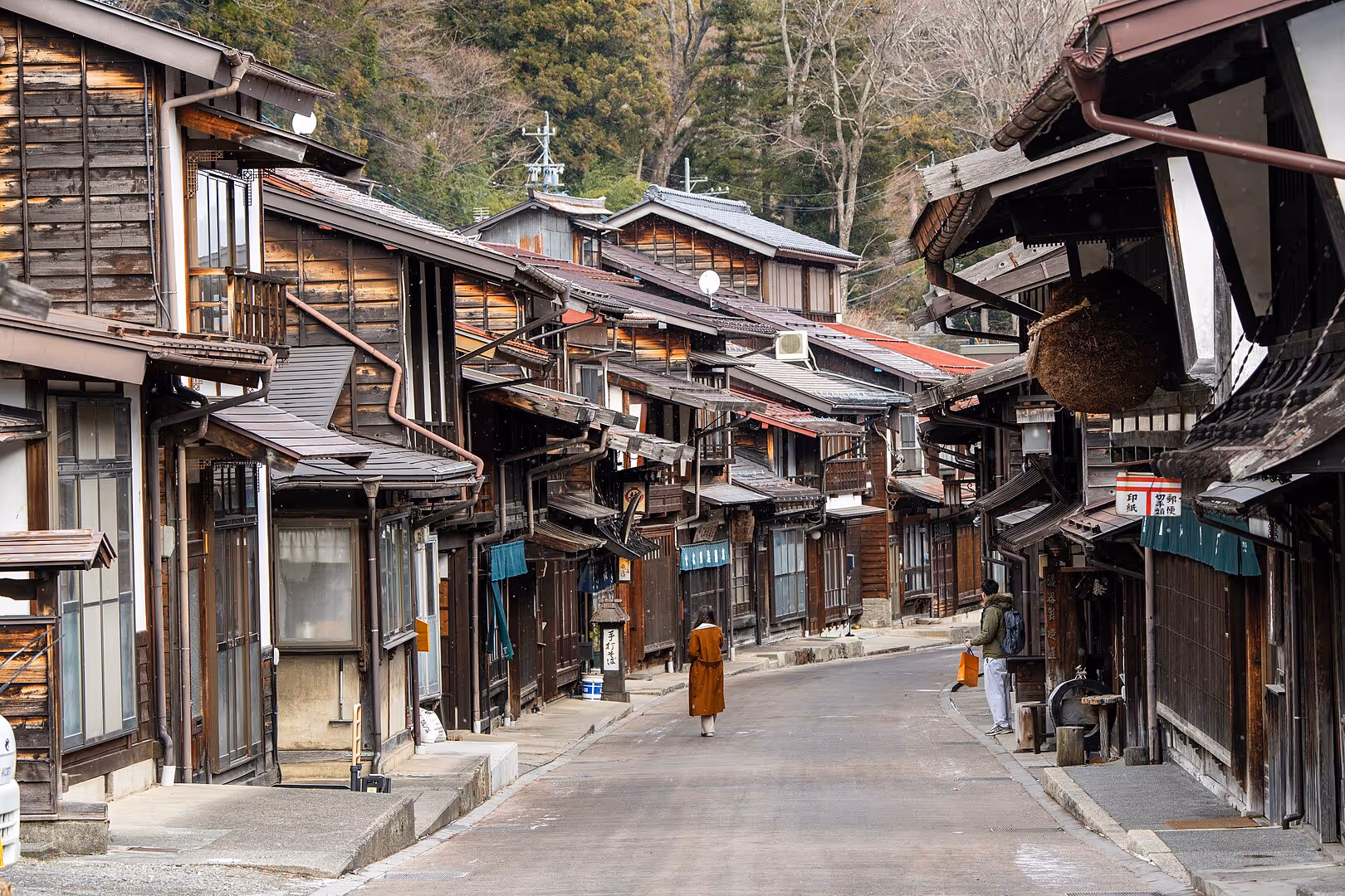 Traditional wooden houses lining a quiet street in a historic Japanese village with two people walking in the distance.