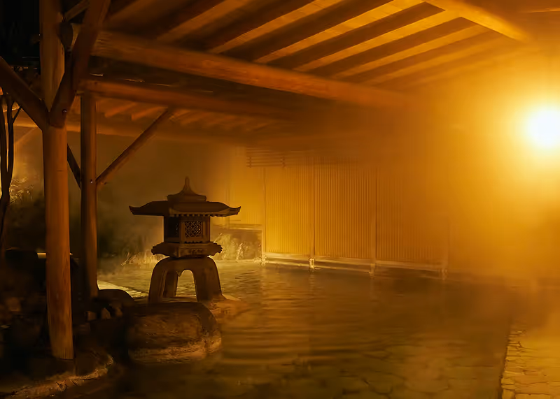 Steamy indoor Japanese onsen with wooden beams, stone lantern, and warm yellow lighting.