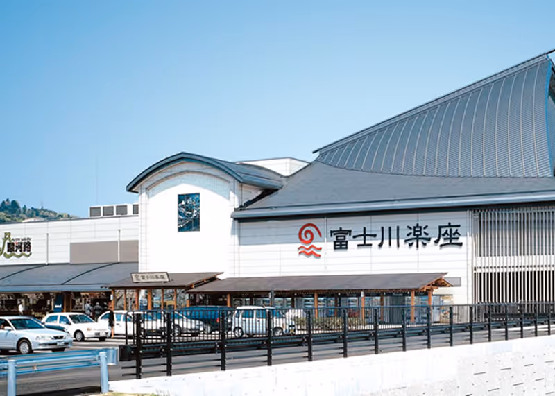 Exterior view of Michi-no-Eki Fujikawa Rakuza roadside station with parked cars and clear blue sky.