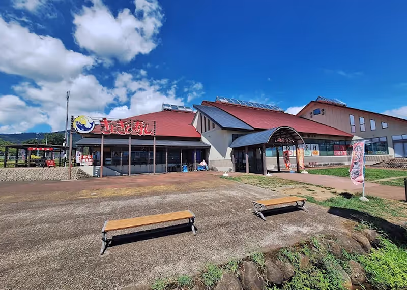 Building with red roofs under a blue sky with clouds, featuring benches and Japanese signage outside.