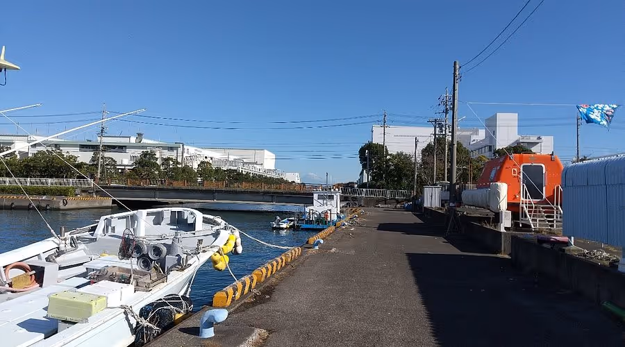 Fishing boats docked at a quiet port with a clear blue sky and industrial buildings in the background.