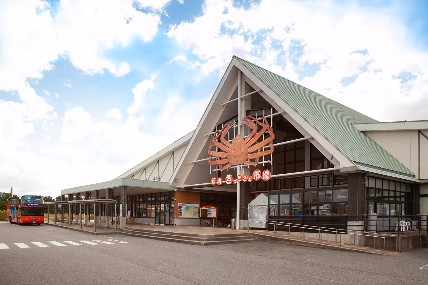 Building with a large crab decoration and Japanese signage above the entrance, a red bus parked nearby under a partly cloudy sky.