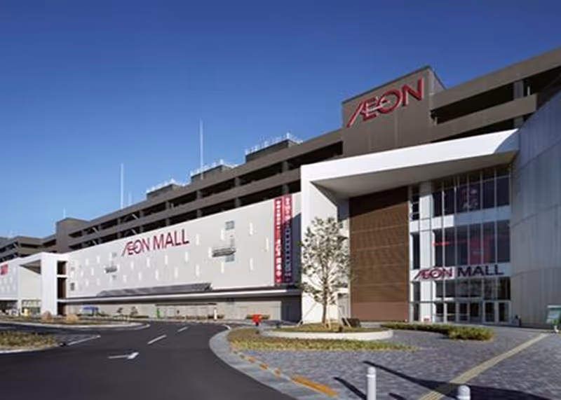 Exterior view of AEON Mall Kusatsu with clear blue sky and a curved road leading to the entrance.