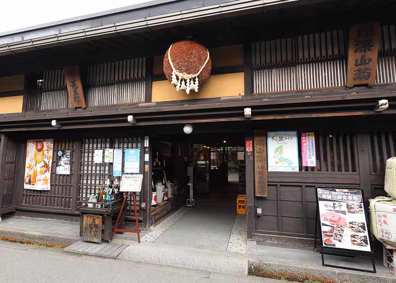 Traditional Japanese building storefront with wooden lattice windows, sake bottles display, and a large round sugidama hanging above the entrance.