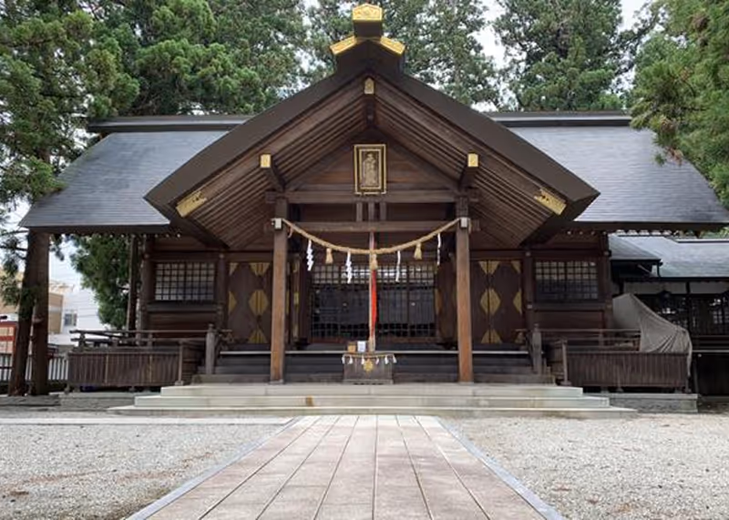 Front view of a traditional Japanese wooden shrine with a rope and paper decorations hanging under the roof peak.