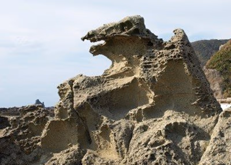 Natural rock formation resembling the silhouette of Godzilla monster at a coastal area.