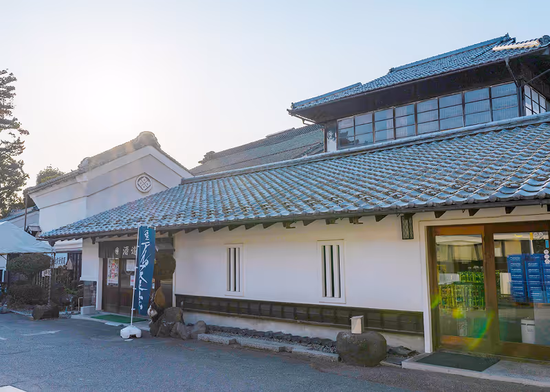 Traditional Japanese sake brewery building with tiled roof and white walls under clear sky.
