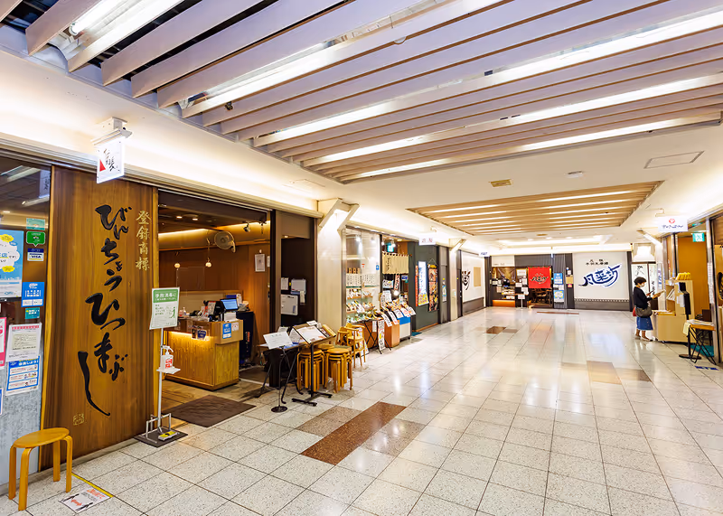 Wide corridor of underground food street with Japanese restaurants and a woman reading a menu on the right.