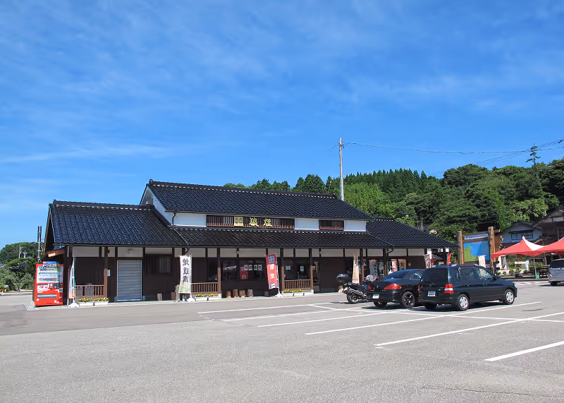 Traditional Japanese building with black tiled roof and parked cars in front under a blue sky.