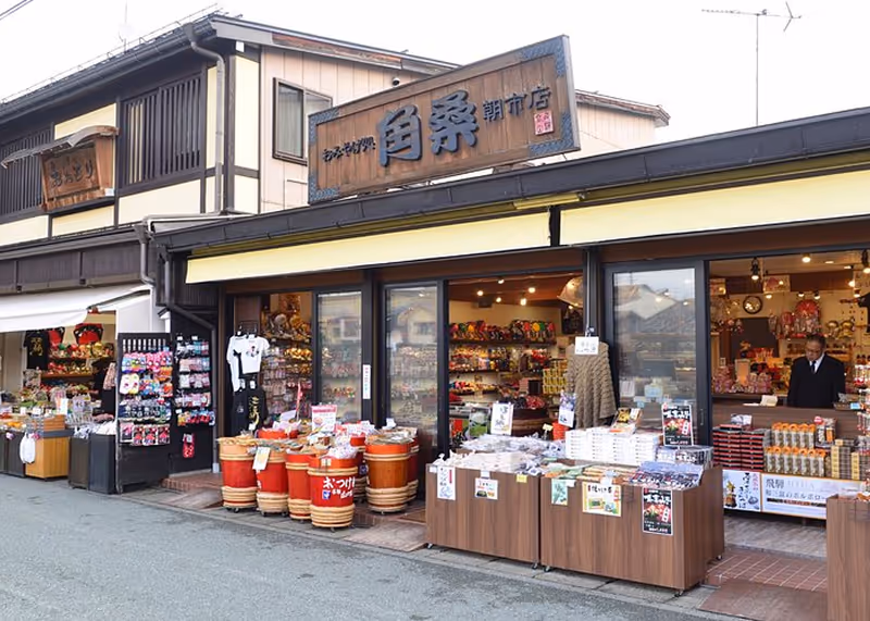 Traditional Japanese storefront with wooden signs and various goods displayed outside on barrels and tables.