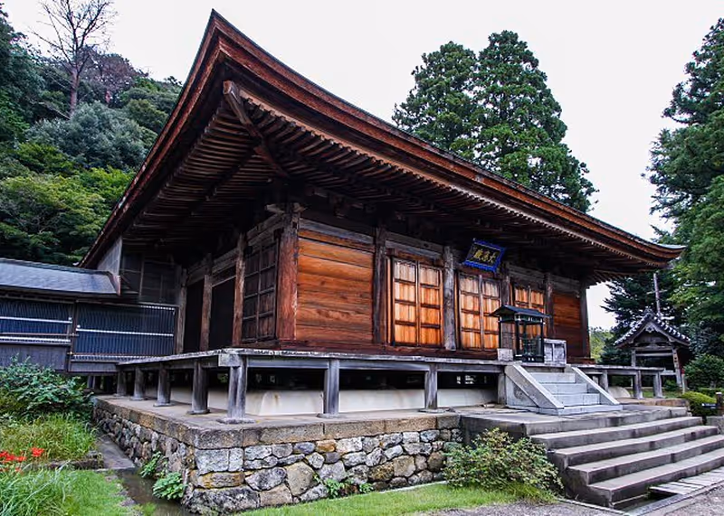 Traditional wooden Japanese temple building elevated on stone foundation with surrounding greenery.