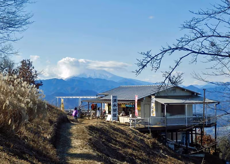 Small mountain tea house on a grassy ridge with distant blue mountains and a partly cloudy sky in the background.