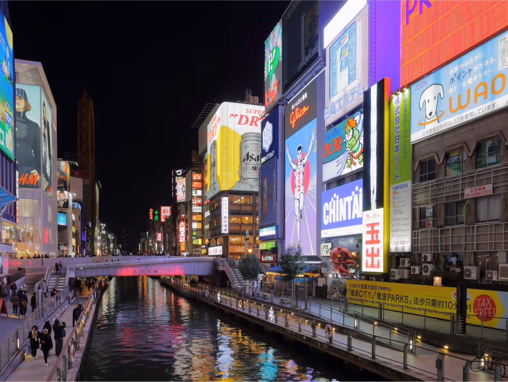 Night view of Dotonbori Canal in Osaka with illuminated colorful billboard advertisements and reflections on the water.